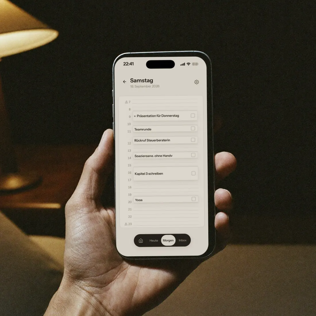 Eine Hand hält ein Handy im Lampenlicht. Auf dem Display steht morgen als Zeitblöcke von 7 bis 23 Uhr.